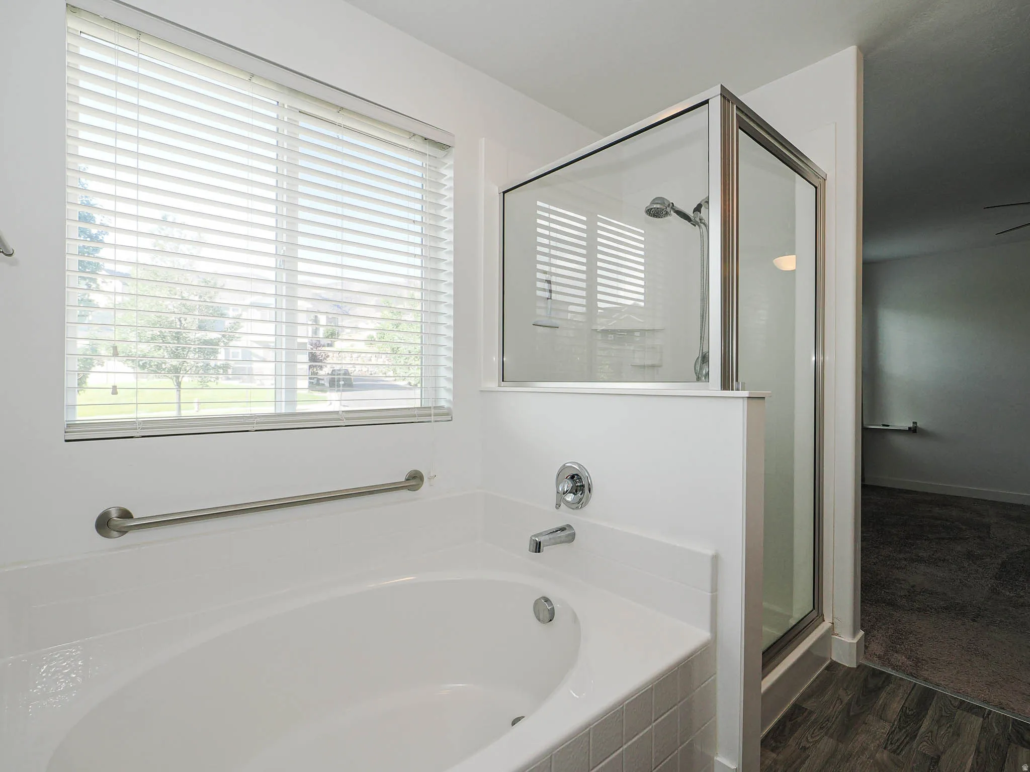 Soaking tub with chrome fixtures, glass-enclosed shower, and a large window with horizontal blinds