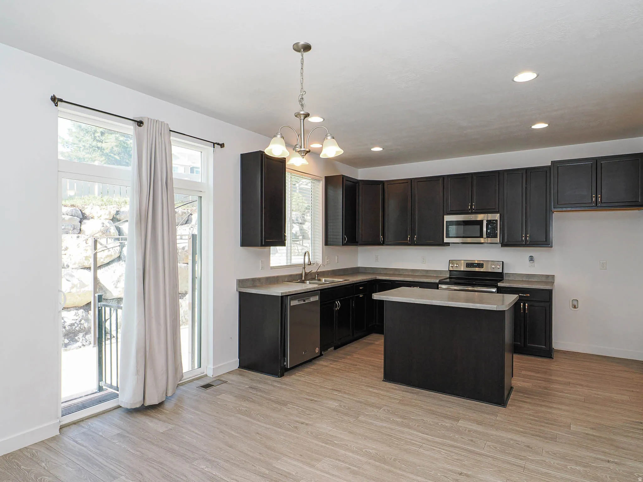 Kitchen featuring dark wood-finish cabinetry, stainless steel appliances, a central island, and wood-finish flooring