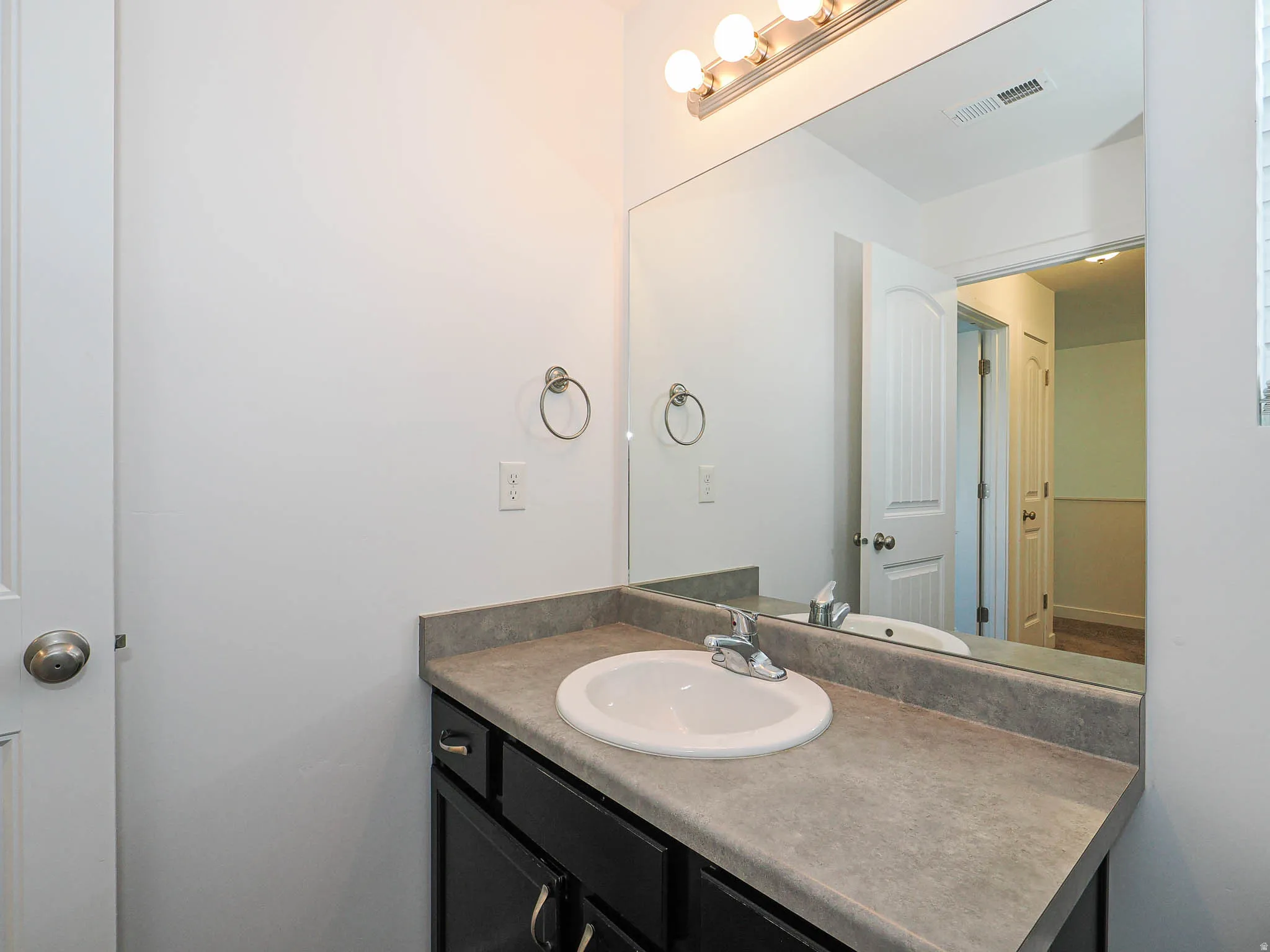 Vanity with a built-in sink, gray countertop, black cabinetry, chrome faucet, and overhead lighting fixture