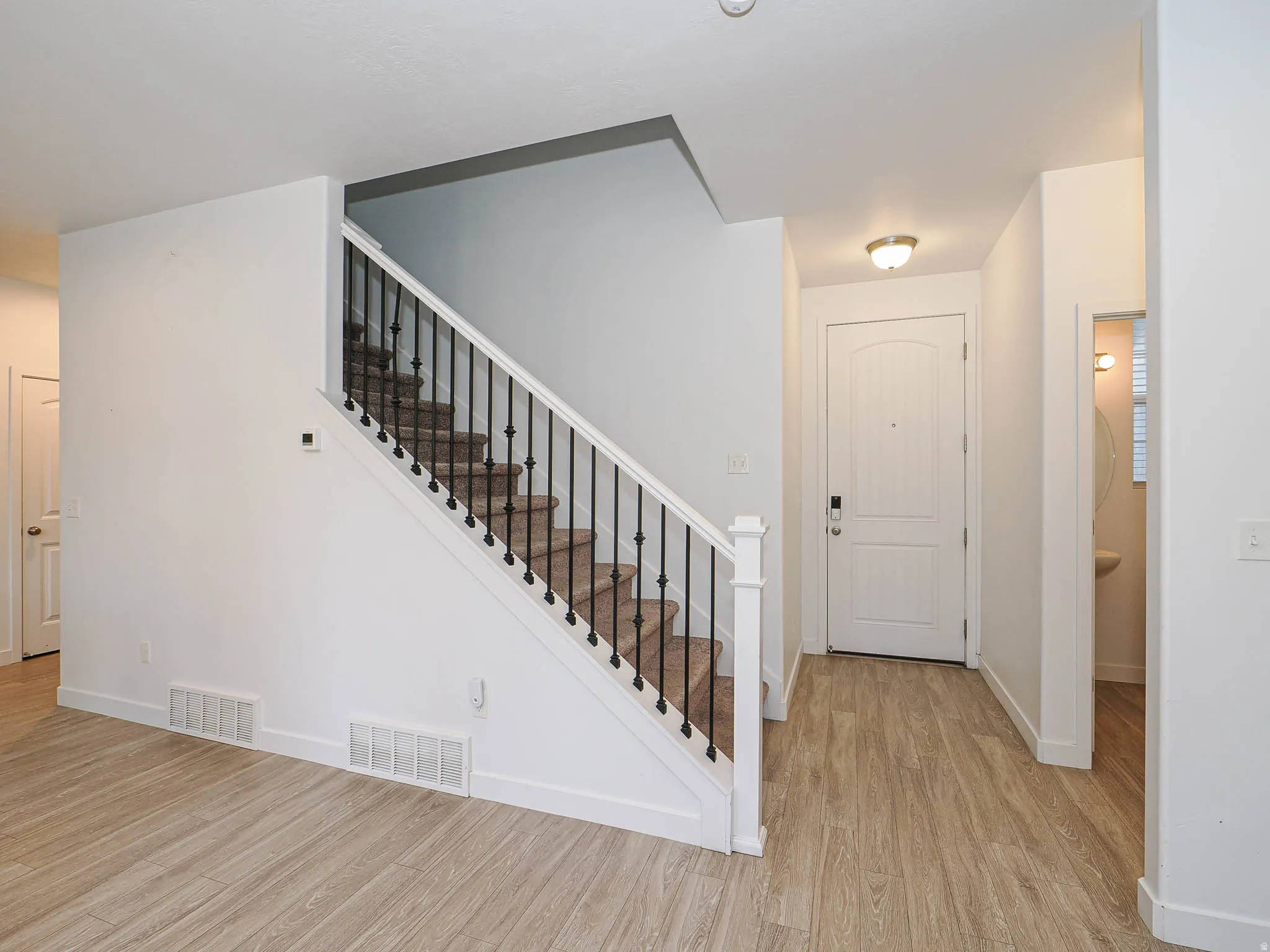 Wood-finish flooring throughout, carpeted staircase with wrought iron balusters, white paneled entry door, and recessed wall paneling