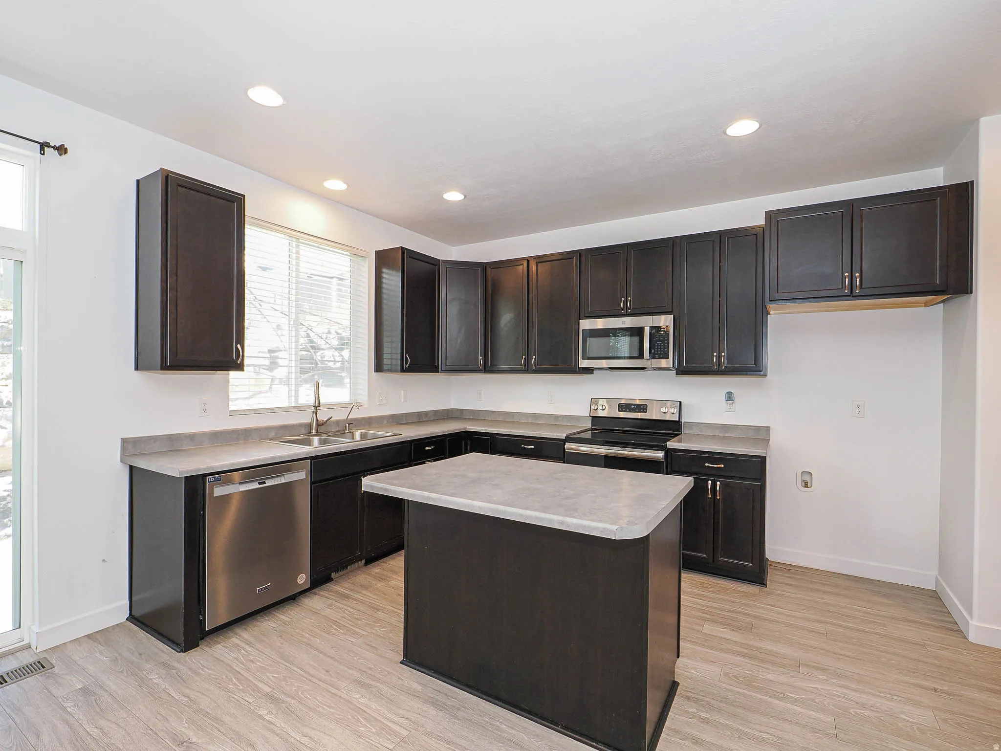 Kitchen featuring dark wood-finish cabinetry, stainless steel appliances, a center island, and wood-finish flooring