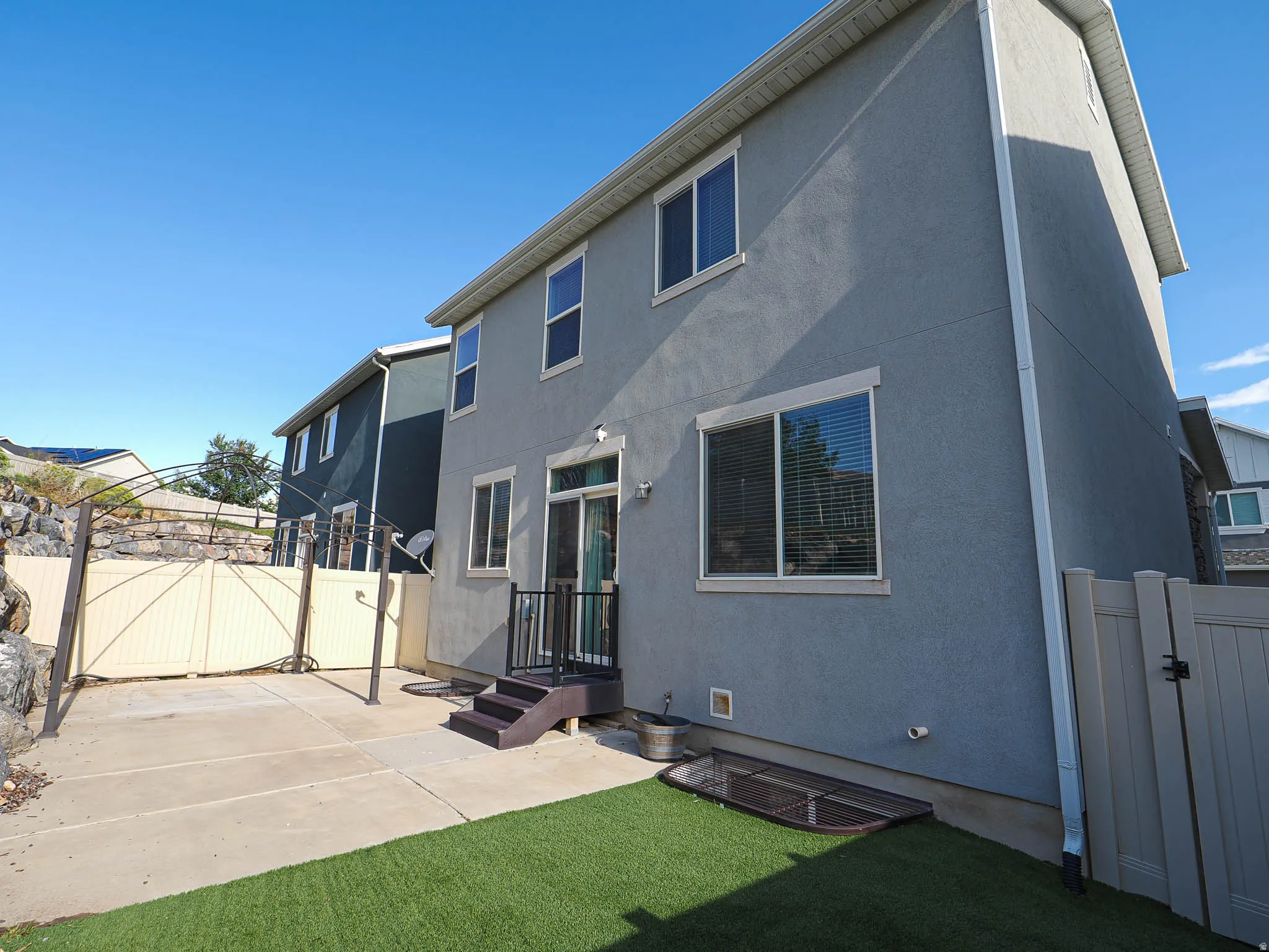 Rear exterior featuring stucco siding, multiple windows, a sliding glass door, a patio area, and a privacy fence