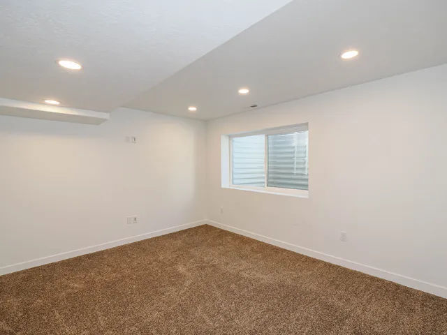 Recessed lighting, brown carpet flooring, white walls, and a white-framed egress window