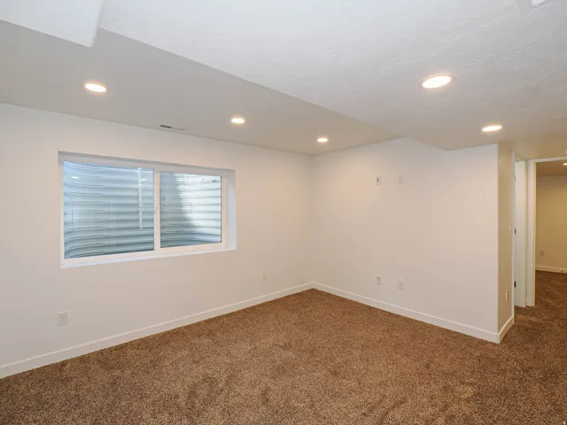 Recessed lighting, white walls, white trim, brown carpeting, and a window with a window well