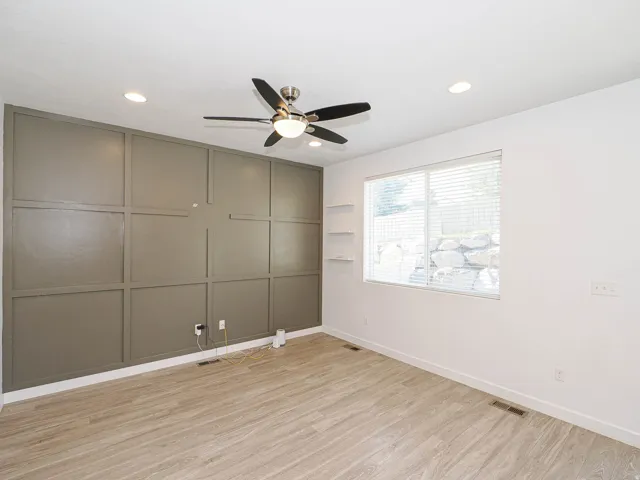 Accent wall with decorative paneling, wood-finish flooring, ceiling fan with light, recessed lighting, and built-in shelving