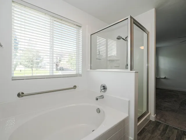 Soaking tub with chrome fixtures, glass-enclosed shower, and a large window with horizontal blinds
