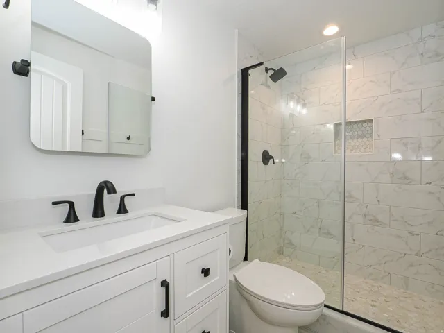 White vanity with a quartz countertop and integrated sink, matte black faucet, and frameless mirror