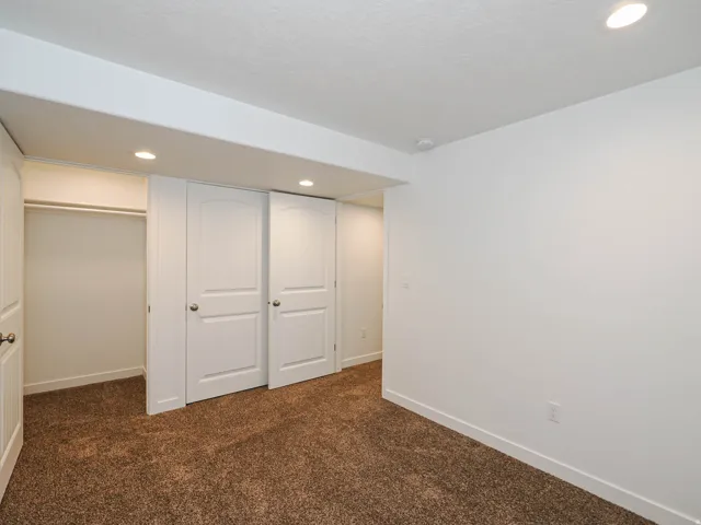 Recessed ceiling lighting, white interior walls, white trim, brown carpet flooring, and white paneled closet doors