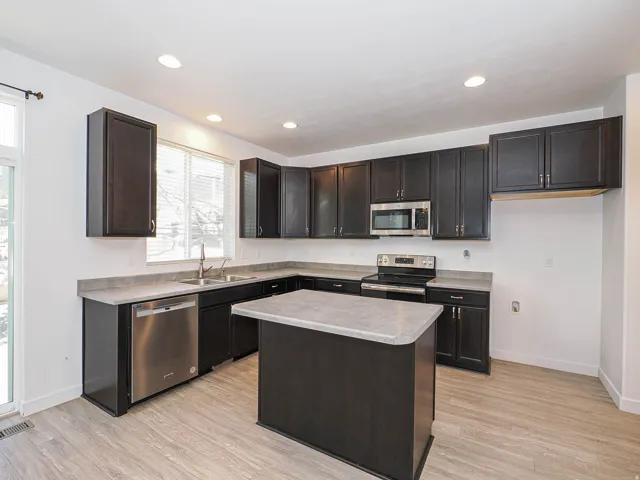 Kitchen featuring dark wood-finish cabinetry, stainless steel appliances, a center island, and wood-finish flooring