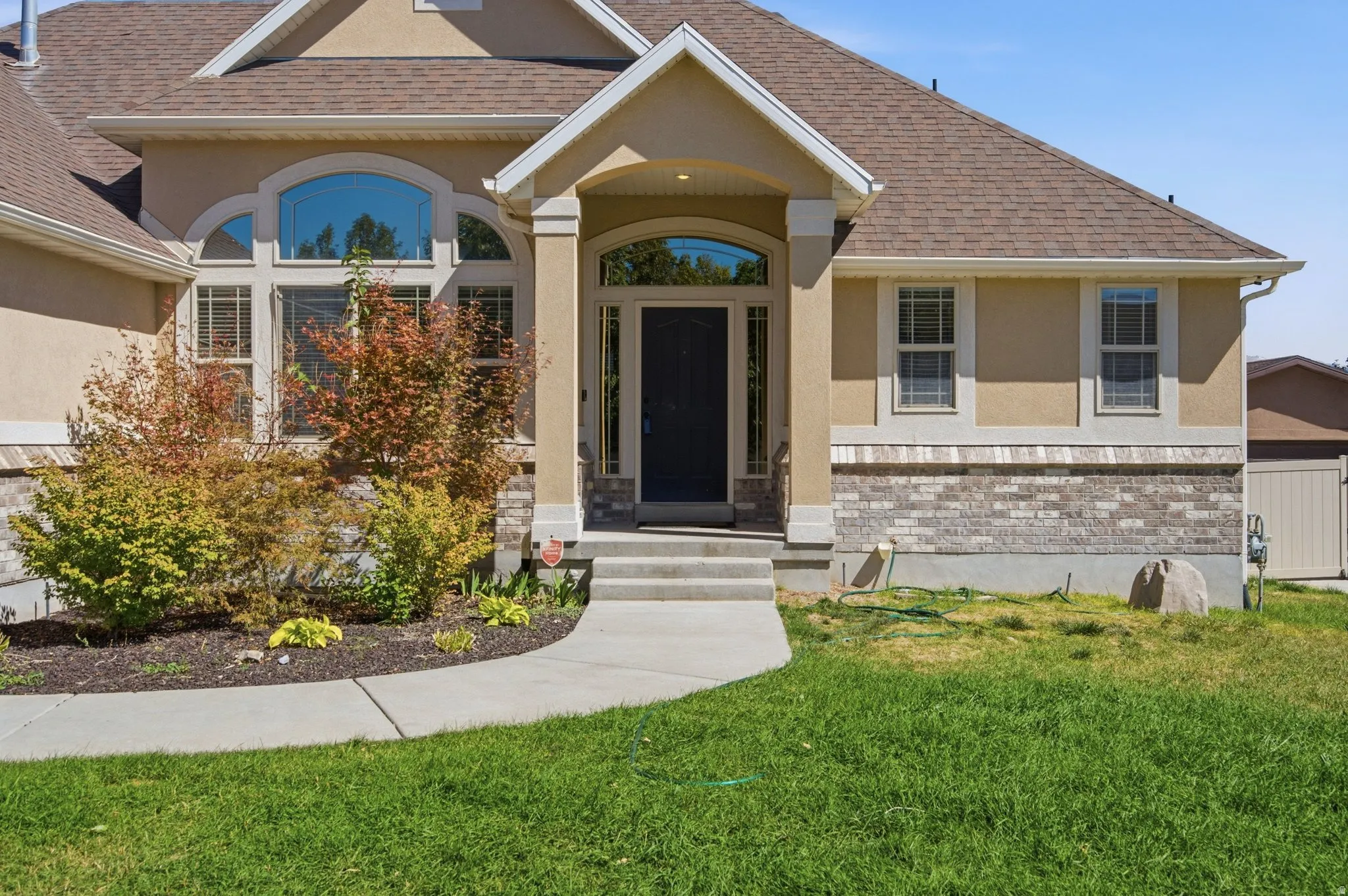 Stucco exterior with stone accent detailing, arched entry, arched window, and concrete pathway