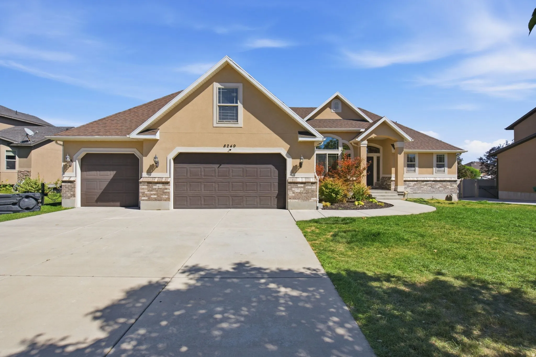 Stucco exterior with stone accents, mature landscaping, and a two-car garage