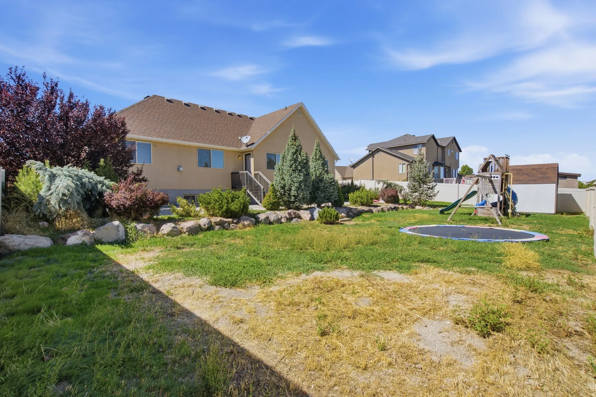 Expansive backyard featuring a stucco exterior, mature landscaping, and a fenced perimeter
