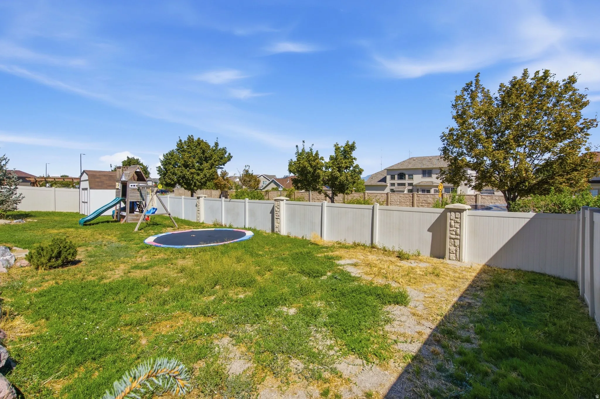 Expansive backyard featuring a vinyl perimeter fence, partial rock landscaping, and mature foliage