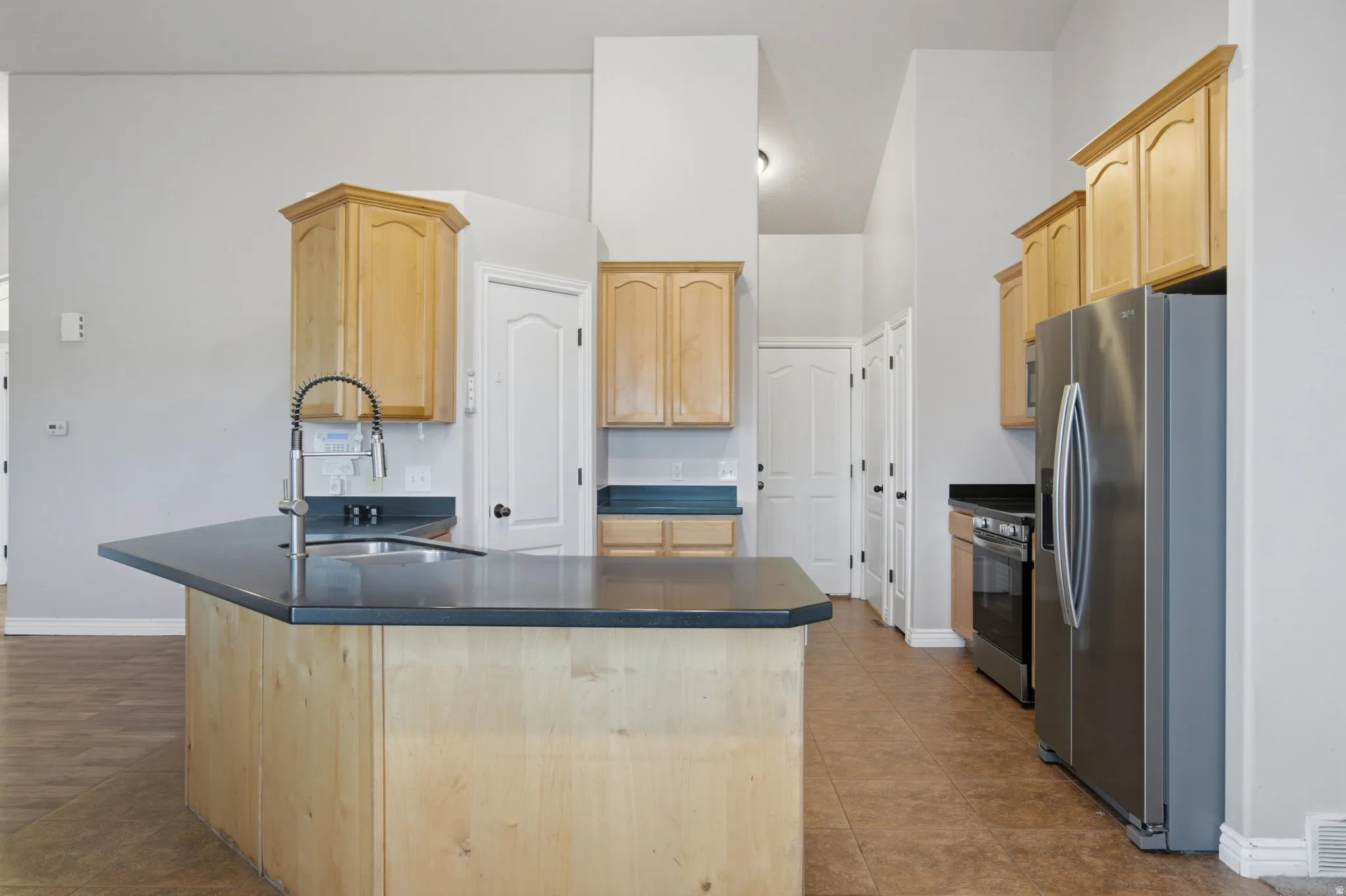 Kitchen featuring a large island with sink, light wood cabinetry, stainless steel appliances, and tile flooring