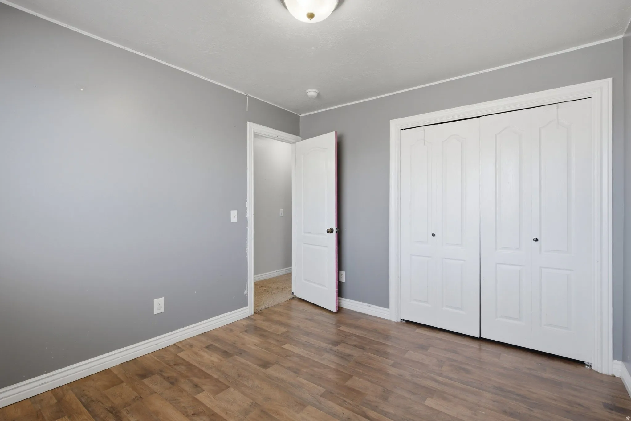 Wood-finish flooring, white bi-fold closet doors, white baseboards, and a semi-flush mount ceiling light fixture