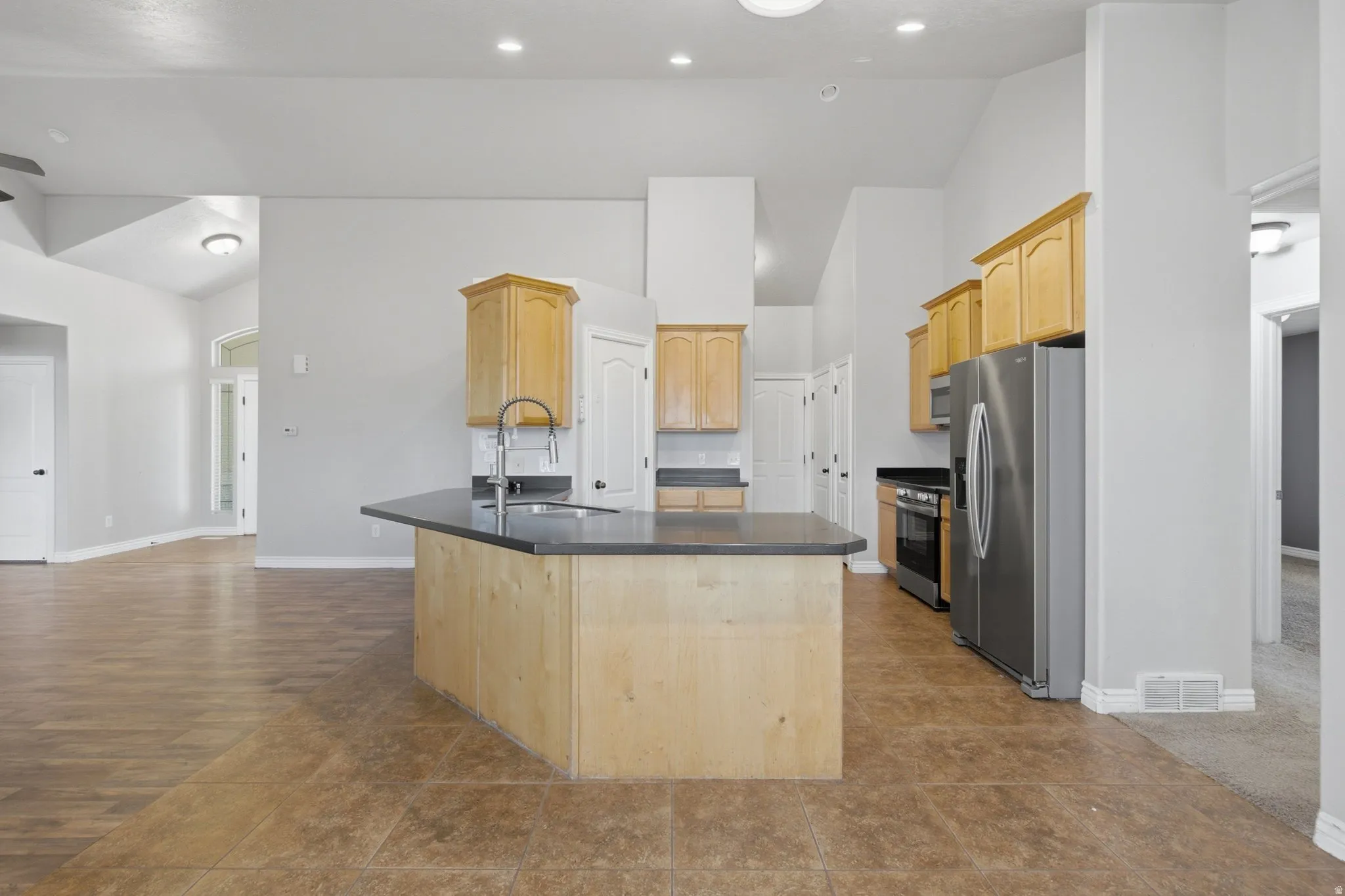 Kitchen featuring light wood-finish cabinetry, stainless steel appliances, and a central island with a dark countertop and integrated sink