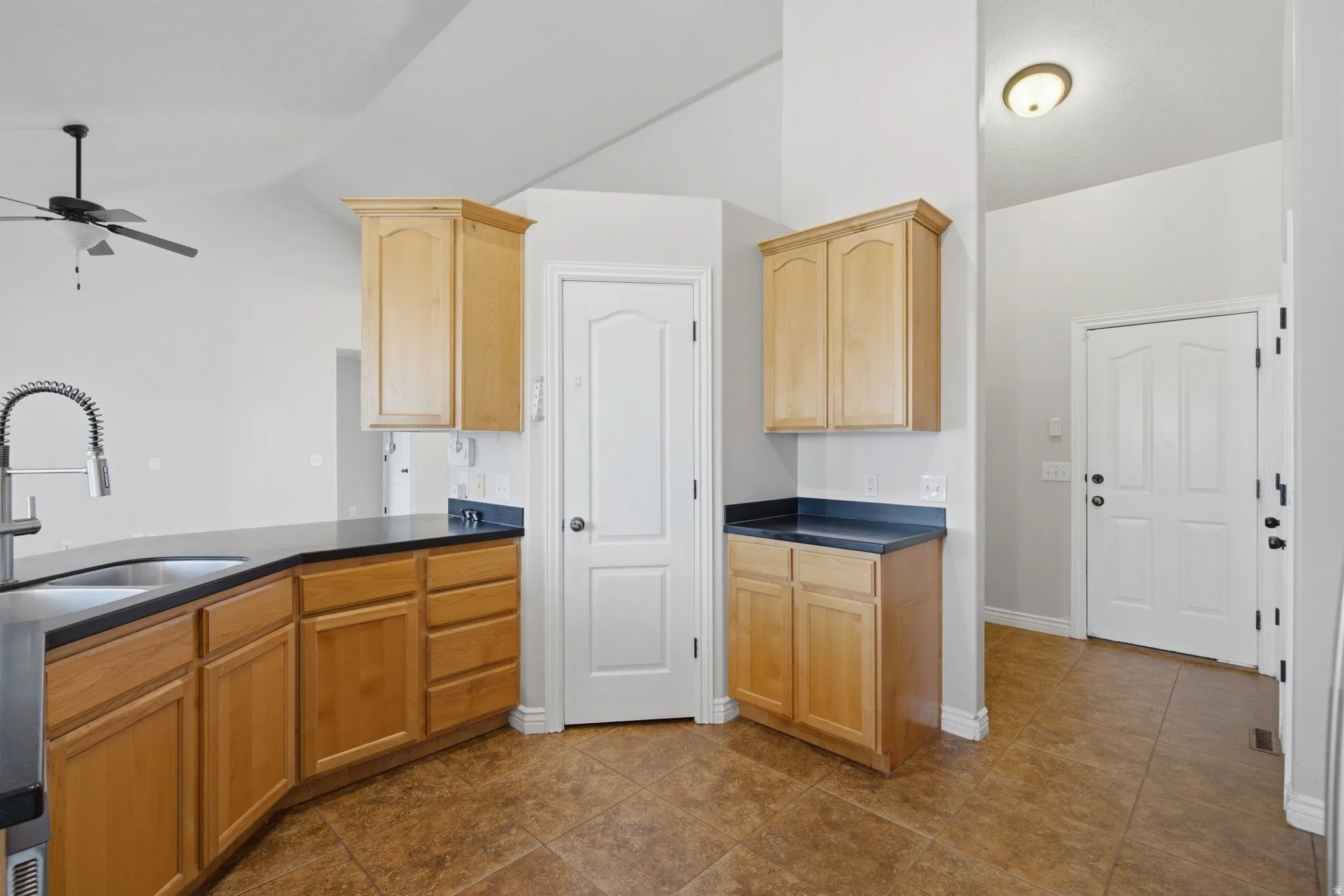 Kitchen with wood-finish cabinetry, black countertops, stainless steel sink, and a high-arch faucet