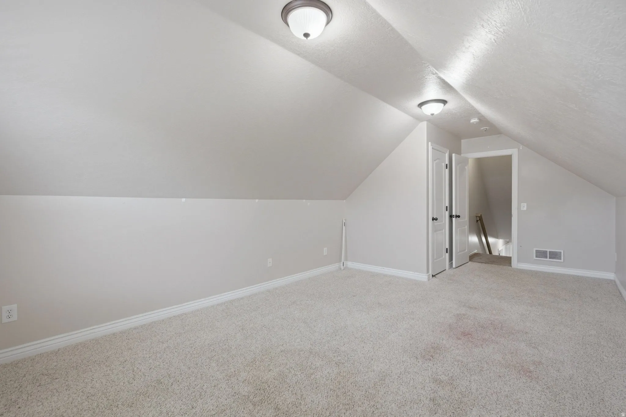 Sloped ceilings, carpeted flooring, two ceiling-mounted light fixtures, white trim, and a white interior door with black hardware