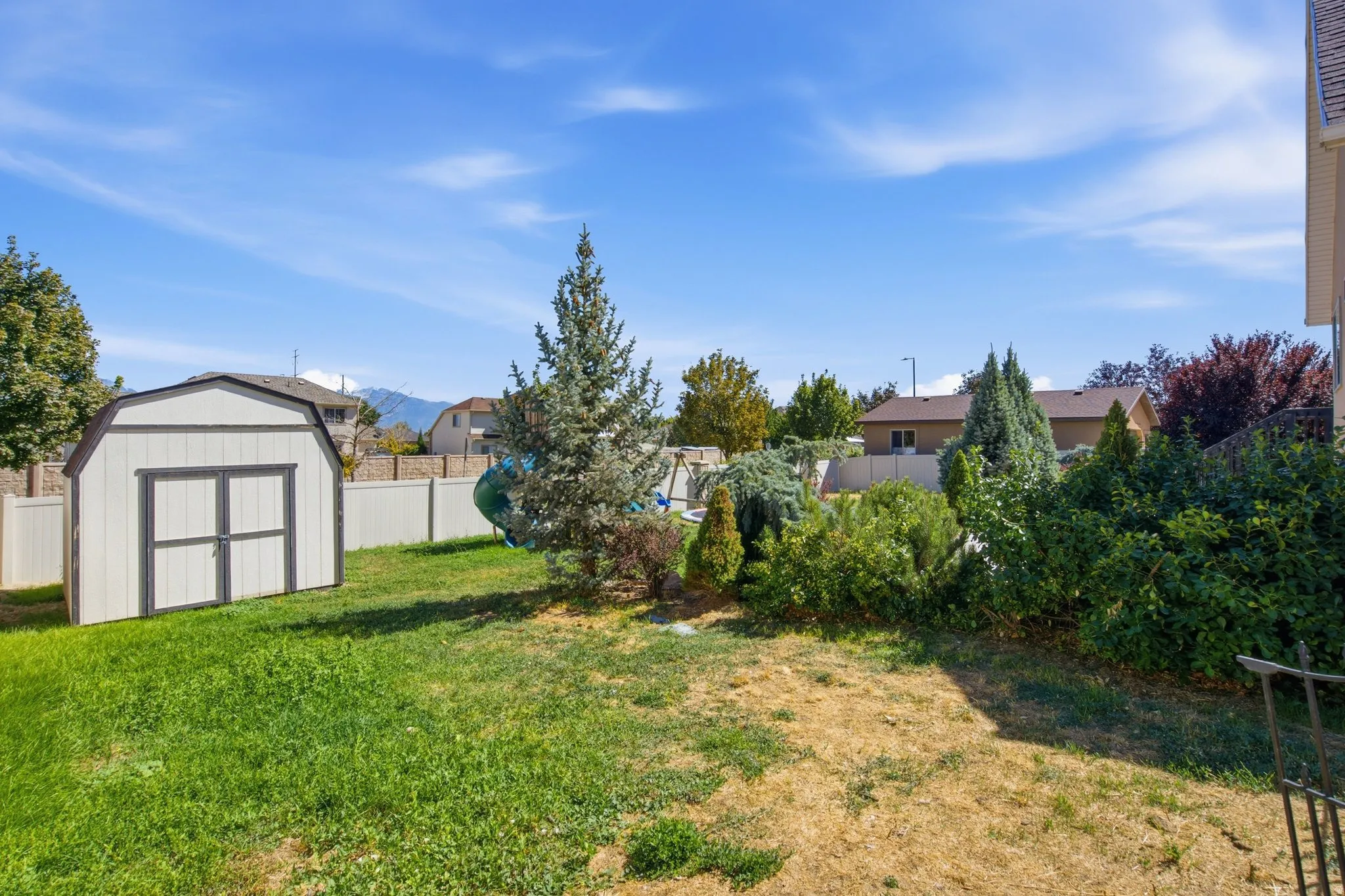 Expansive backyard with a storage shed, white vinyl fencing, and mature landscaping