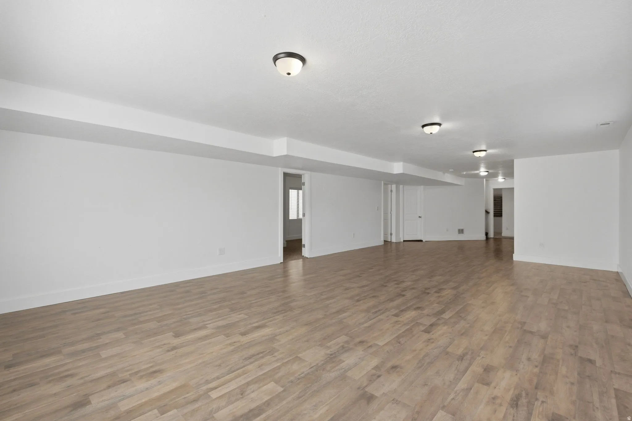Expansive room featuring wood-finish flooring, recessed ceiling, and multiple flush-mount light fixtures