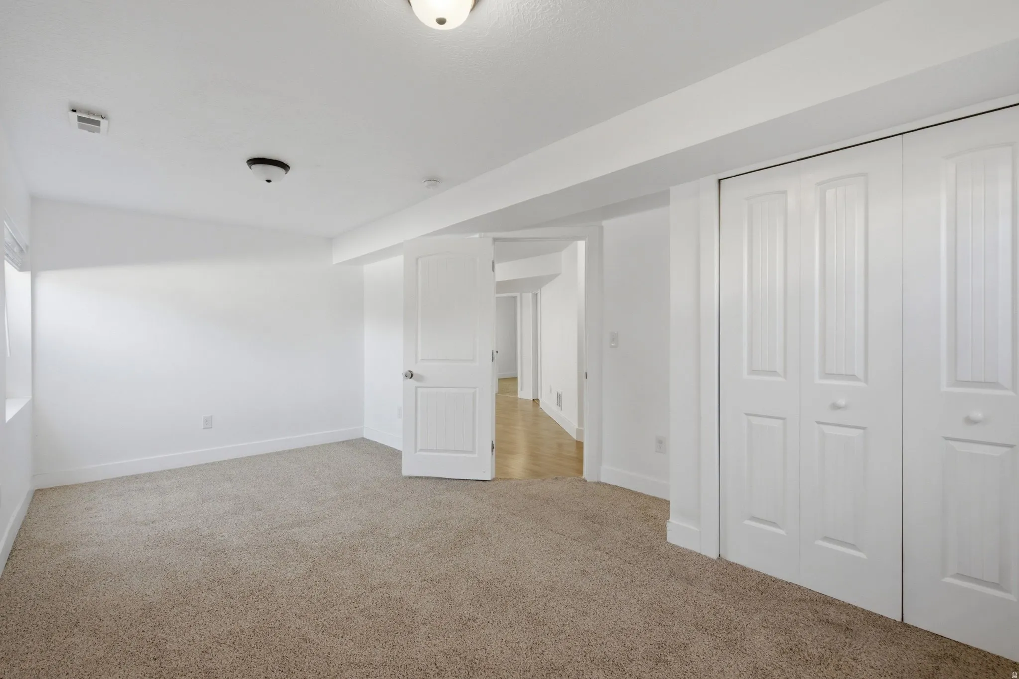 Neutral tone wall color, carpeted flooring, window opening, white paneled door, and bi-fold closet doors