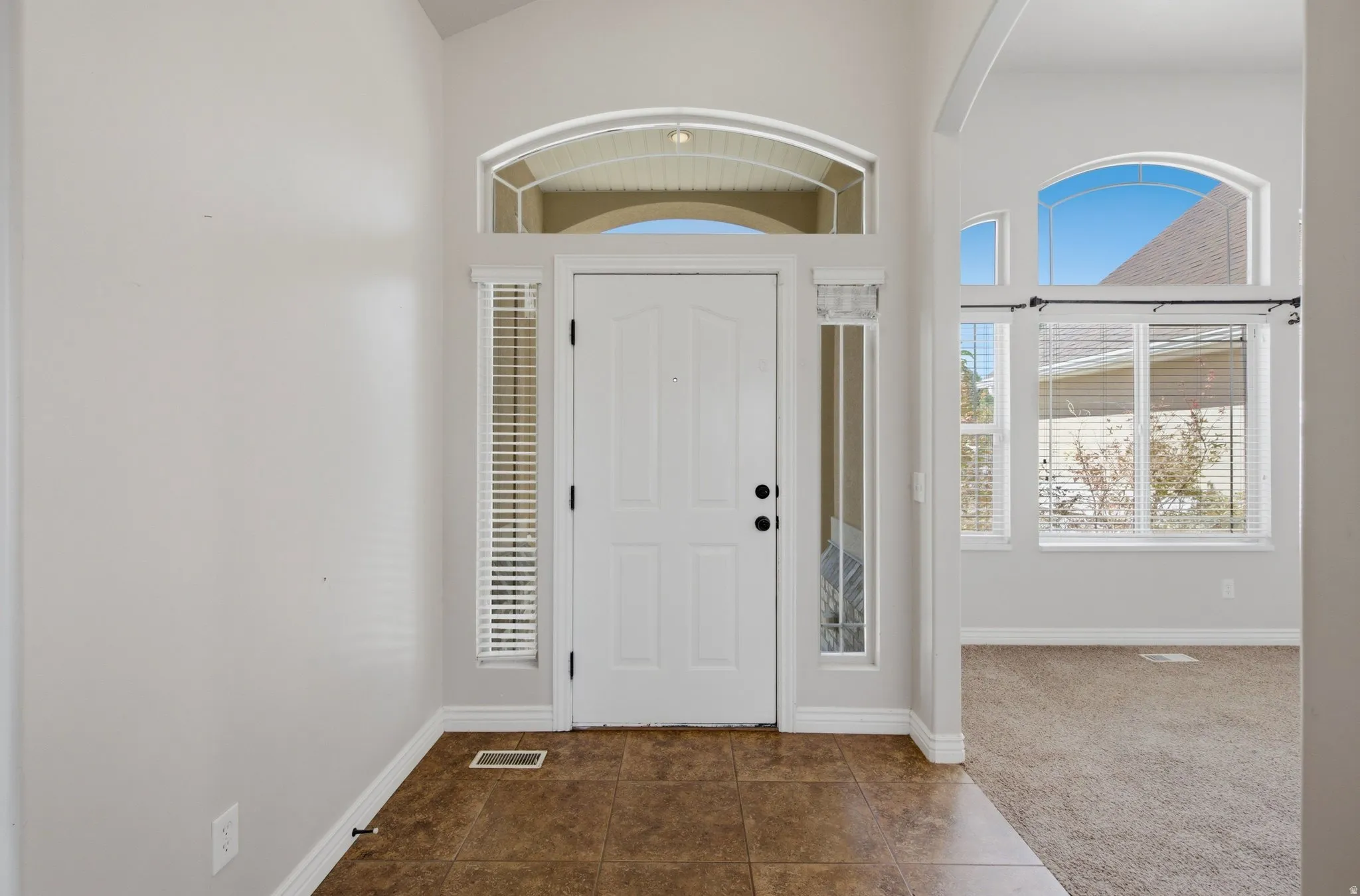 Entryway featuring tile flooring, a white paneled door, decorative transom window, and sidelight windows
