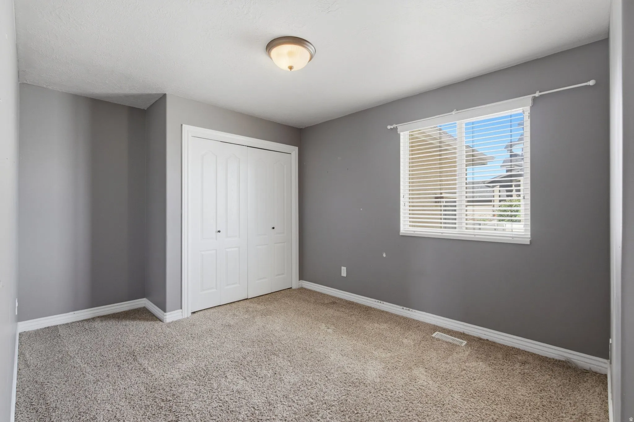 Neutral-toned walls, carpeted flooring, and a window with blinds