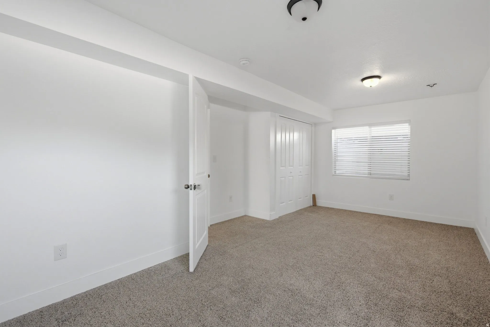 Recessed lighting, neutral tone carpeting, white bi-fold closet doors, white window blinds, and a semi-flush mount ceiling light fixture