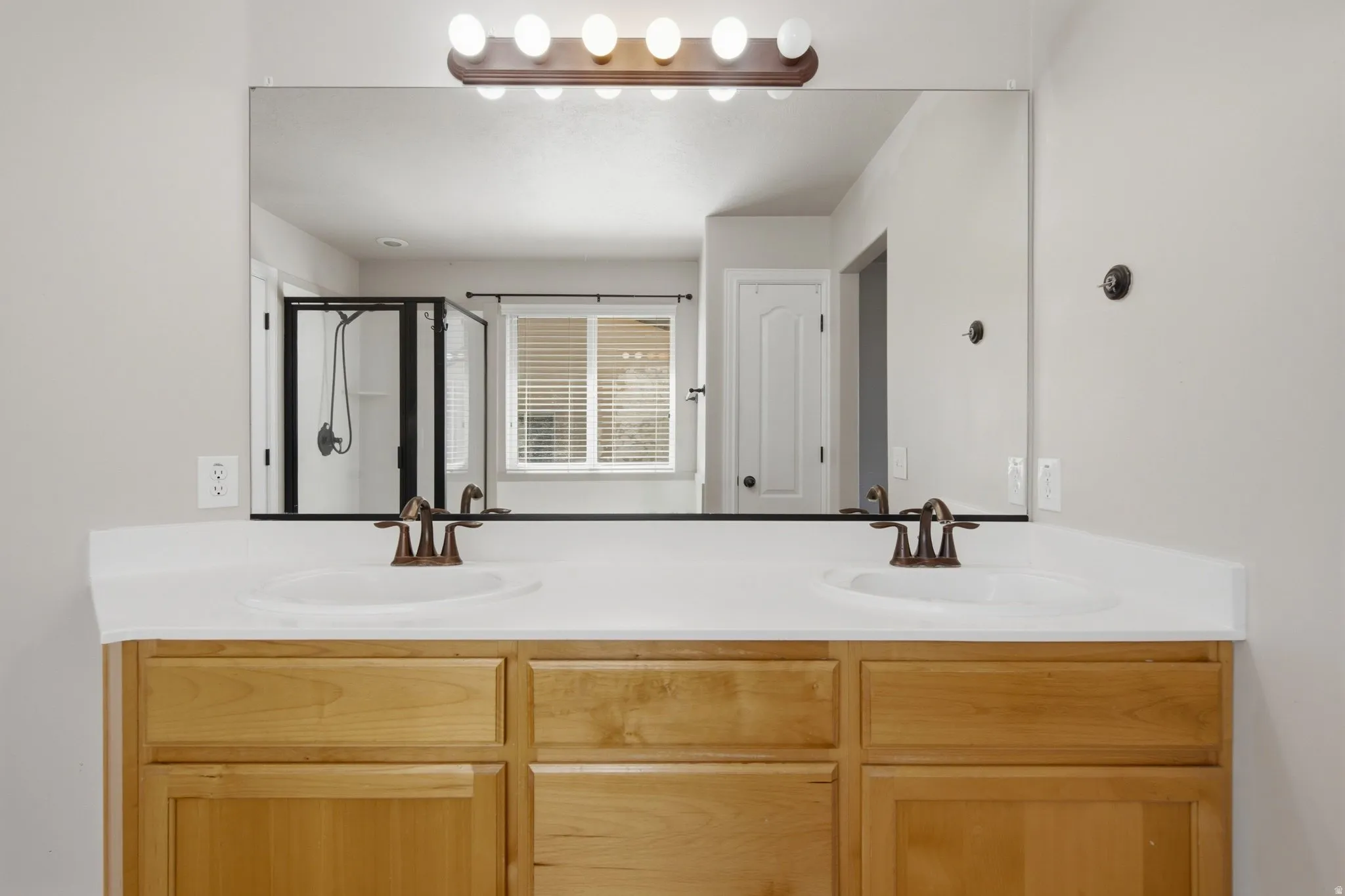 Dual vanity with light wood-finish cabinetry, integrated sinks, and bronze-finish faucets