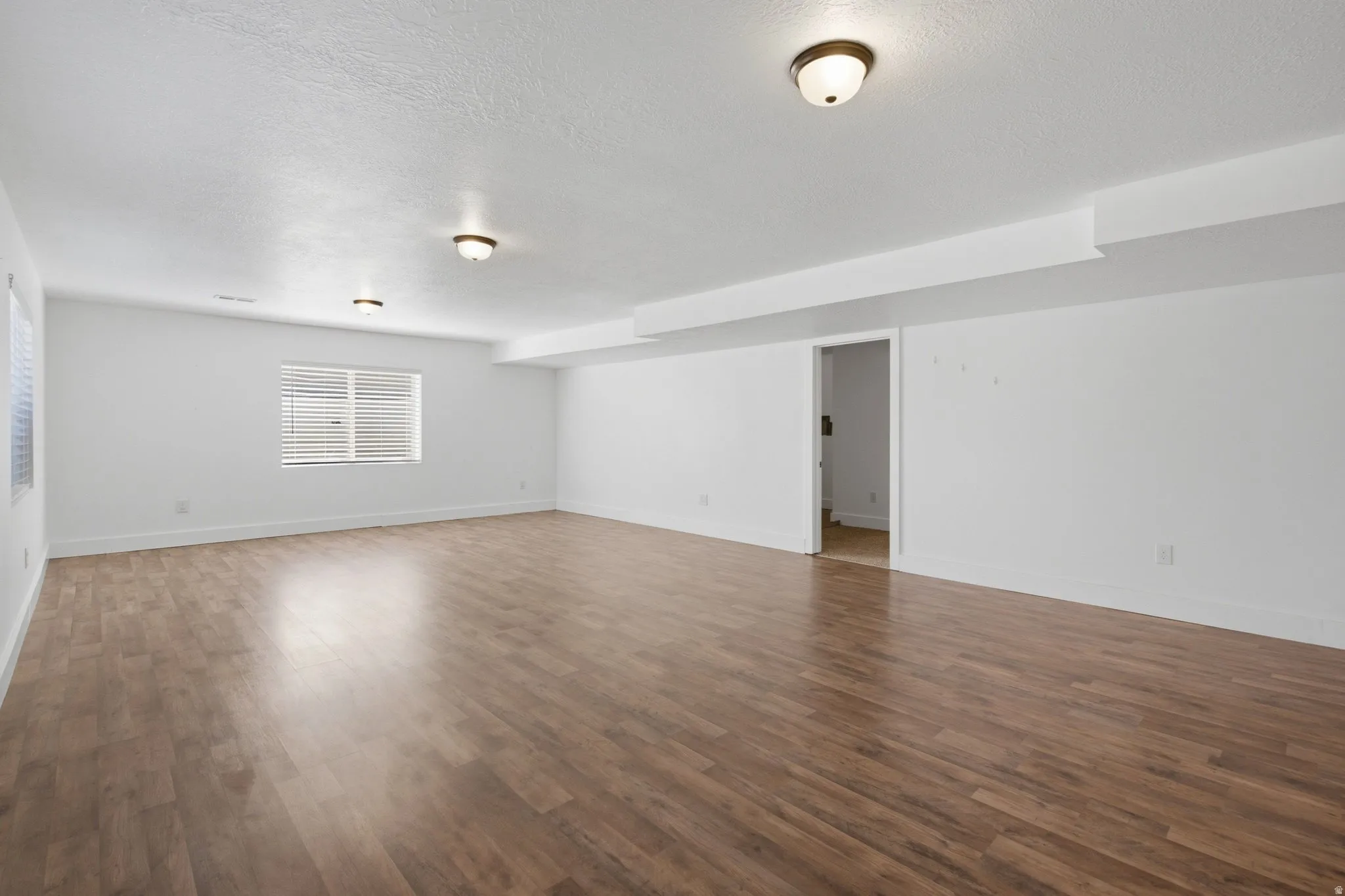 Spacious room featuring wood-finish flooring, white walls, and multiple windows with blinds