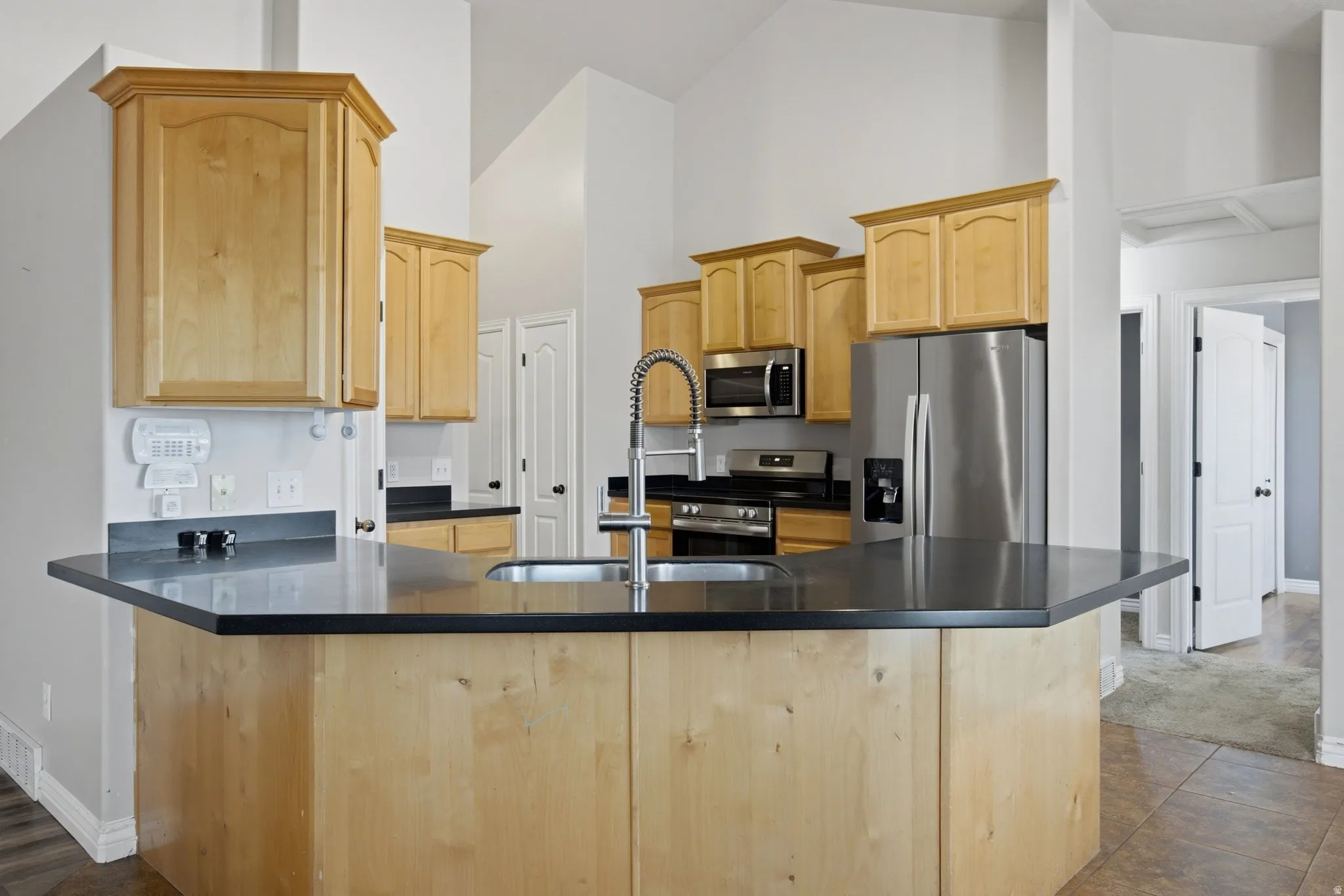 Kitchen featuring light wood cabinetry, dark countertops, a stainless steel refrigerator, stainless steel microwave, and a stainless steel range