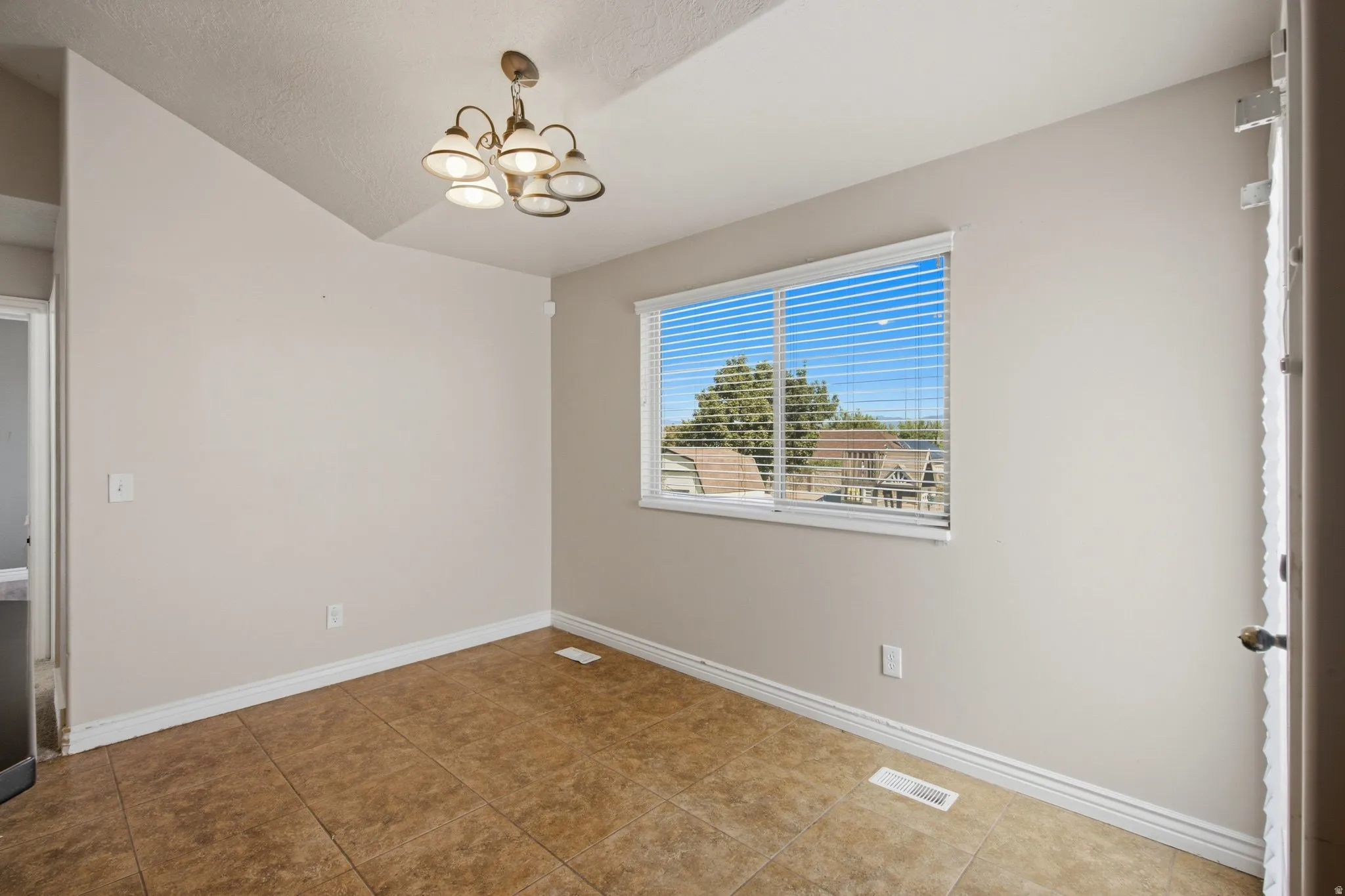 Neutral wall tones, window with horizontal blinds, overhead chandelier, and tile flooring