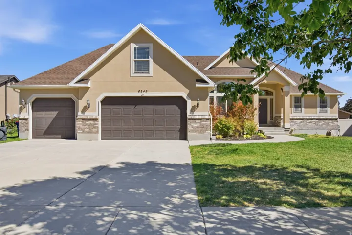 Stucco exterior with brick veneer accents, two attached garage doors, concrete driveway, and front landscaping