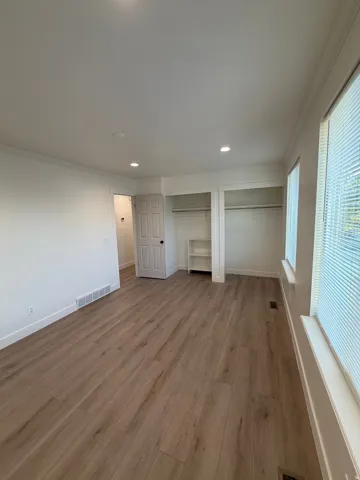 Wood-finish flooring, recessed ceiling lighting, built-in shelving, and two windows with blinds