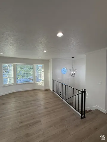 Recessed lighting, wood-finish flooring, bay window with blinds, black metal railing, and a decorative chandelier