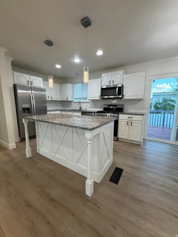Kitchen featuring a center island with granite-style countertop, white cabinetry, wood-finish flooring, and recessed lighting