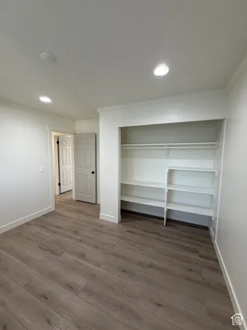 Wood-finish flooring, recessed ceiling lighting, built-in closet shelving, crown molding, and paneled doors