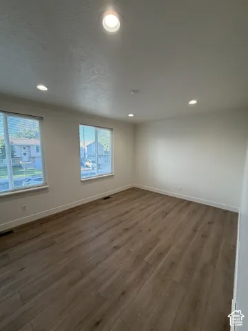 Interior room featuring wood-finish flooring, neutral wall paint, dual windows, and recessed lighting
