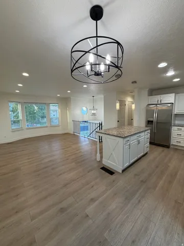 Wood-finish flooring, recessed lighting, bay window, kitchen island with granite-style countertop, and stainless steel appliances