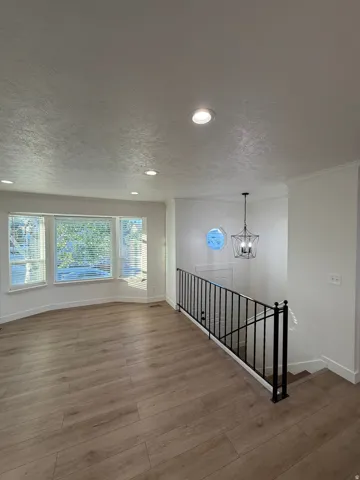 Recessed lighting, wood-finish flooring, bay window with blinds, black metal railing, and a decorative chandelier