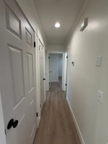 Recessed lighting, wood-finish flooring, white paneled doors with matte black hardware, and crown molding