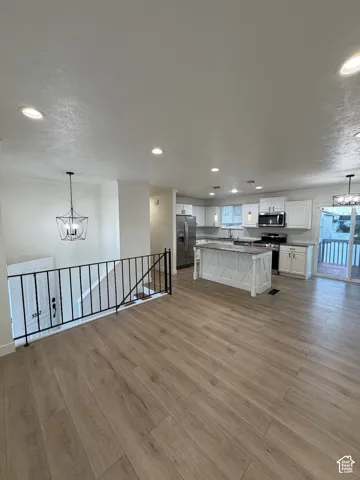 Open-concept living area featuring wood-finish flooring, recessed lighting, and a kitchen with white cabinetry and stainless steel appliances