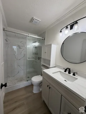 Bathroom featuring a walk-in shower with glass sliding doors, stone-finish wall tile, wood-finish flooring, vanity with a white countertop, and a circular wall-mounted mirror