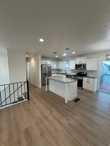 Wood-finish flooring throughout, white cabinetry, stainless steel appliances, granite countertops, and a kitchen island with decorative paneling
