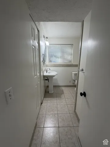 Pedestal sink with chrome faucet, wall-mounted light fixture, and horizontal window blinds