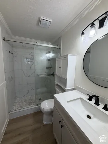 Bathroom featuring a white vanity with a rectangular basin, matte black faucet, walk-in shower with sliding glass doors and large-format tile surround, hexagonal tile shower floor, and wood-finish flooring