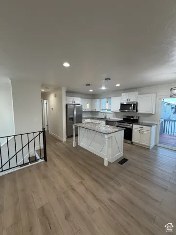 Wood-finish flooring throughout, white cabinetry, stainless steel appliances, granite countertops, and a kitchen island with decorative paneling