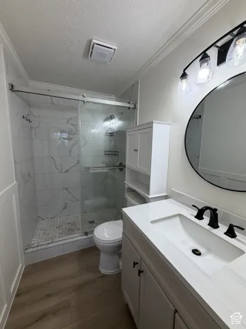 Modern bathroom featuring a glass-enclosed shower with subway tile surround and mosaic floor, a single vanity with an integrated sink and matte black faucet, and wood-finish flooring