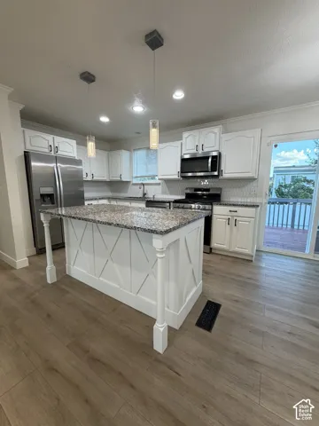 Kitchen featuring white cabinetry, stone countertops, a center island with X-detailing, stainless steel appliances, and wood-finish flooring