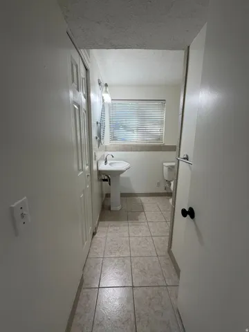 Pedestal sink with chrome faucet, wall-mounted light fixture, and horizontal window blinds